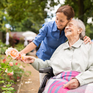 Senior woman sitting on a wheelchair with caregiver, walking in a park